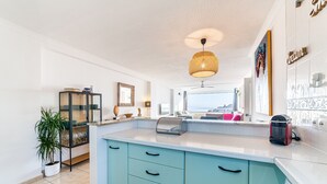 Une cuisine avec un plan de travail blanc, des armoires de couleur turquoise, un luminaire suspendu et une vue sur l’extérieur.