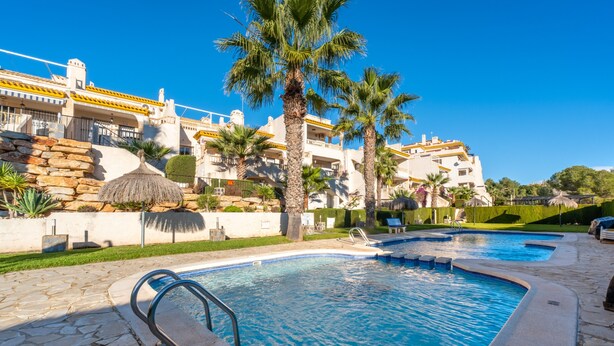 A swimming pool with a stone deck, palm trees, and a building with balconies in the background. - Nice Apartment in a Wonderful Area with Shared Pool & Wi-Fi (Las Ramblas)