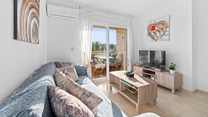 A modern living room with a sofa, TV, and a sliding glass door leading to an outdoor area. - Nice Apartment in a Wonderful Area with Shared Pool & Wi-Fi (Las Ramblas)