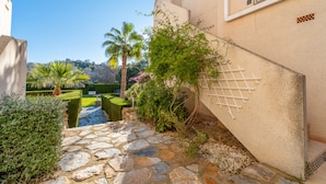 A stone pathway leading to a building with a white lattice structure, surrounded by well-maintained greenery and a clear blue sky. - Nice Apartment in a Wonderful Area with Shared Pool & Wi-Fi (Las Ramblas)
