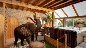 Un intérieur en bois avec un mur en pierre, un escalier en bois, un jacuzzi et une sculpture d’éléphant en bois.