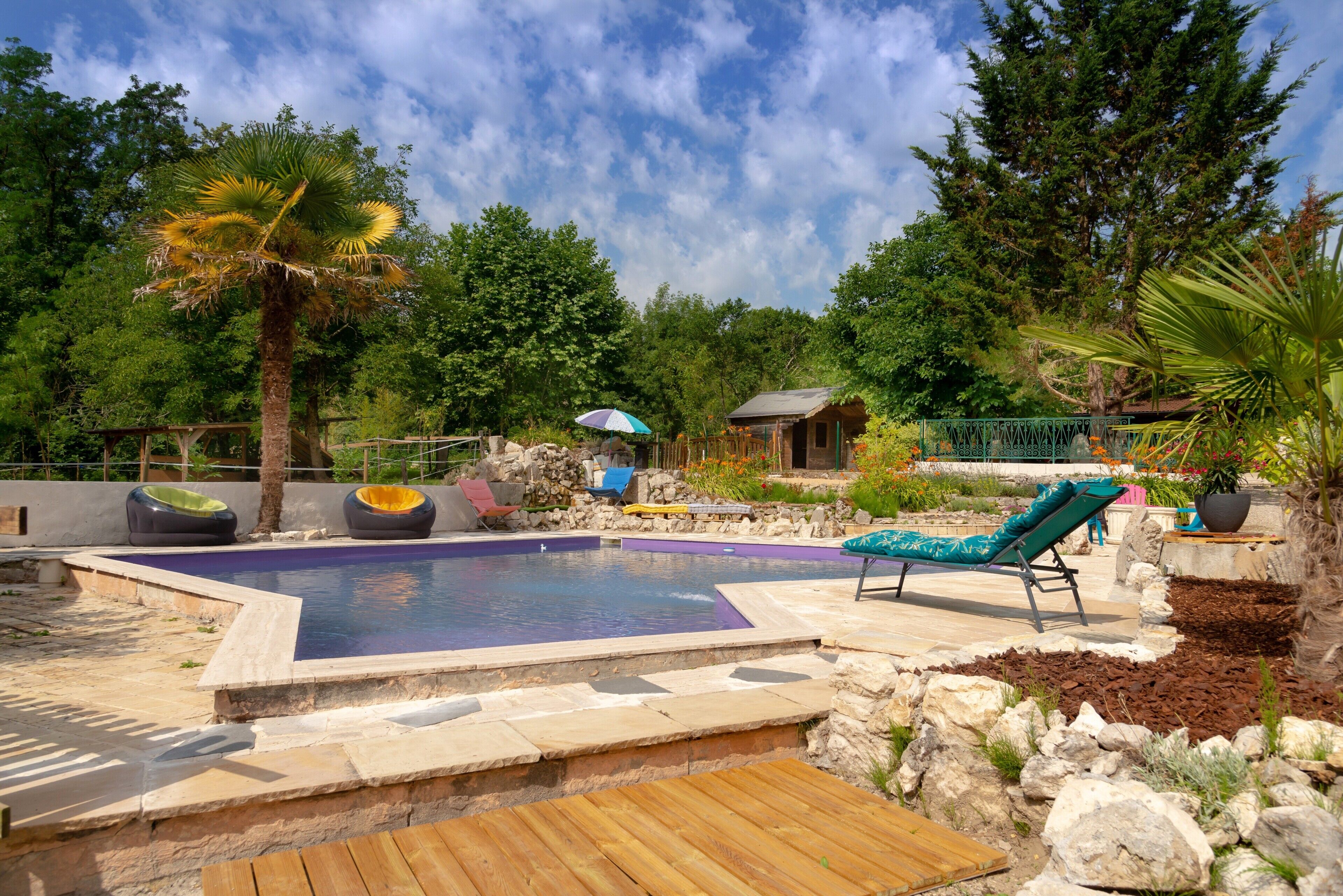 A swimming pool with lounge chairs, a wooden deck, and a stone wall.