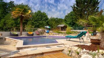 A swimming pool with lounge chairs, a wooden deck, and a stone wall.
