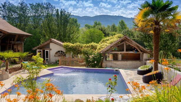 Une piscine dotée d’une terrasse en bois, entourée de verdure et avec une chaîne de montagnes en toile de fond.