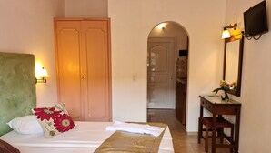 Una camera d'albergo con un letto, una scrivania, una sedia, una TV e un bagno visibile attraverso un arco.