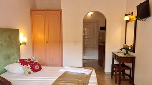 A hotel room with a bed, a desk, a chair, a TV, and a bathroom visible through an archway.