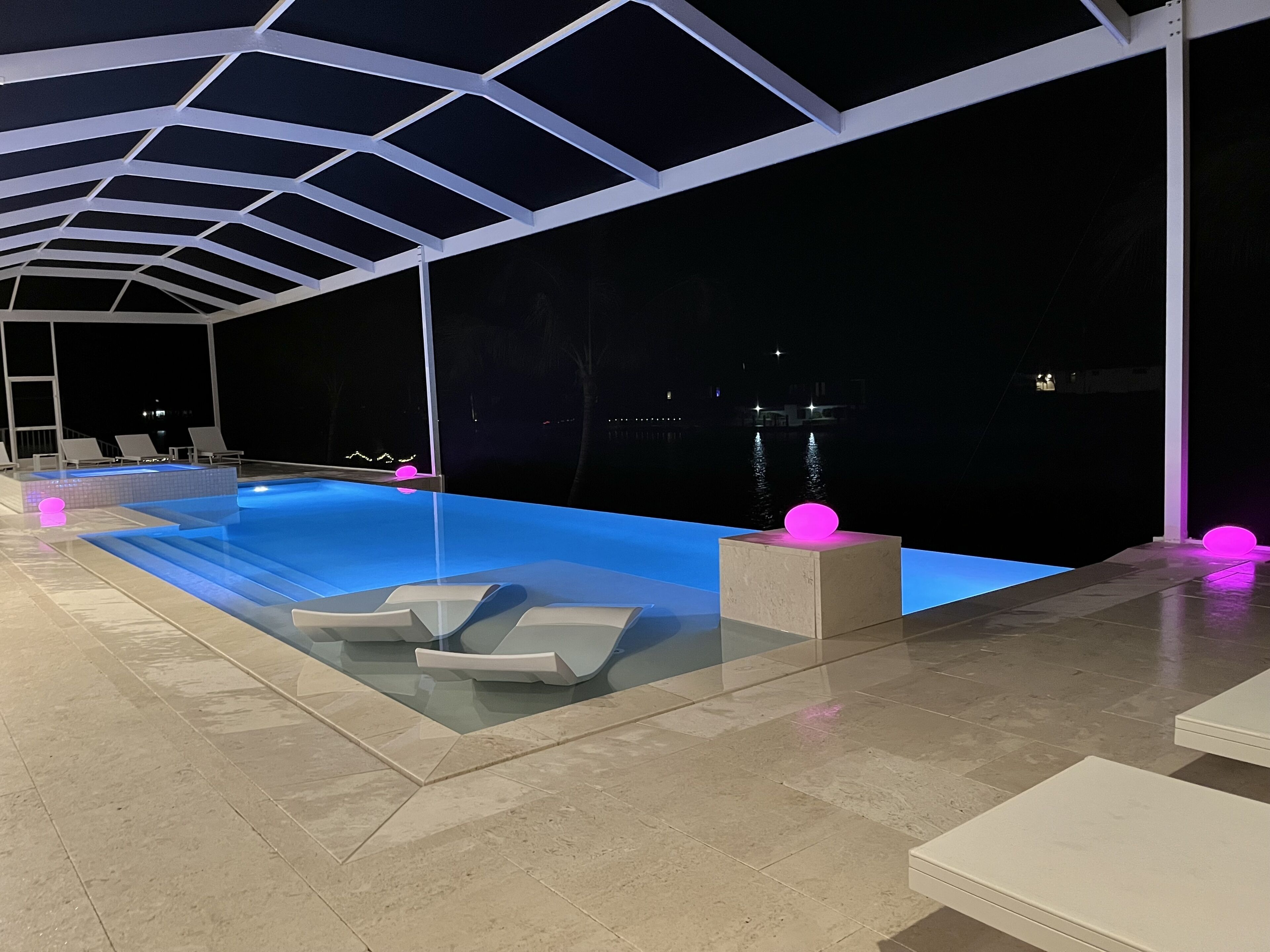 Een buitenzwembad met een modern ontwerp, inclusief geometrische plafondconstructies en verlichte roze bollen.