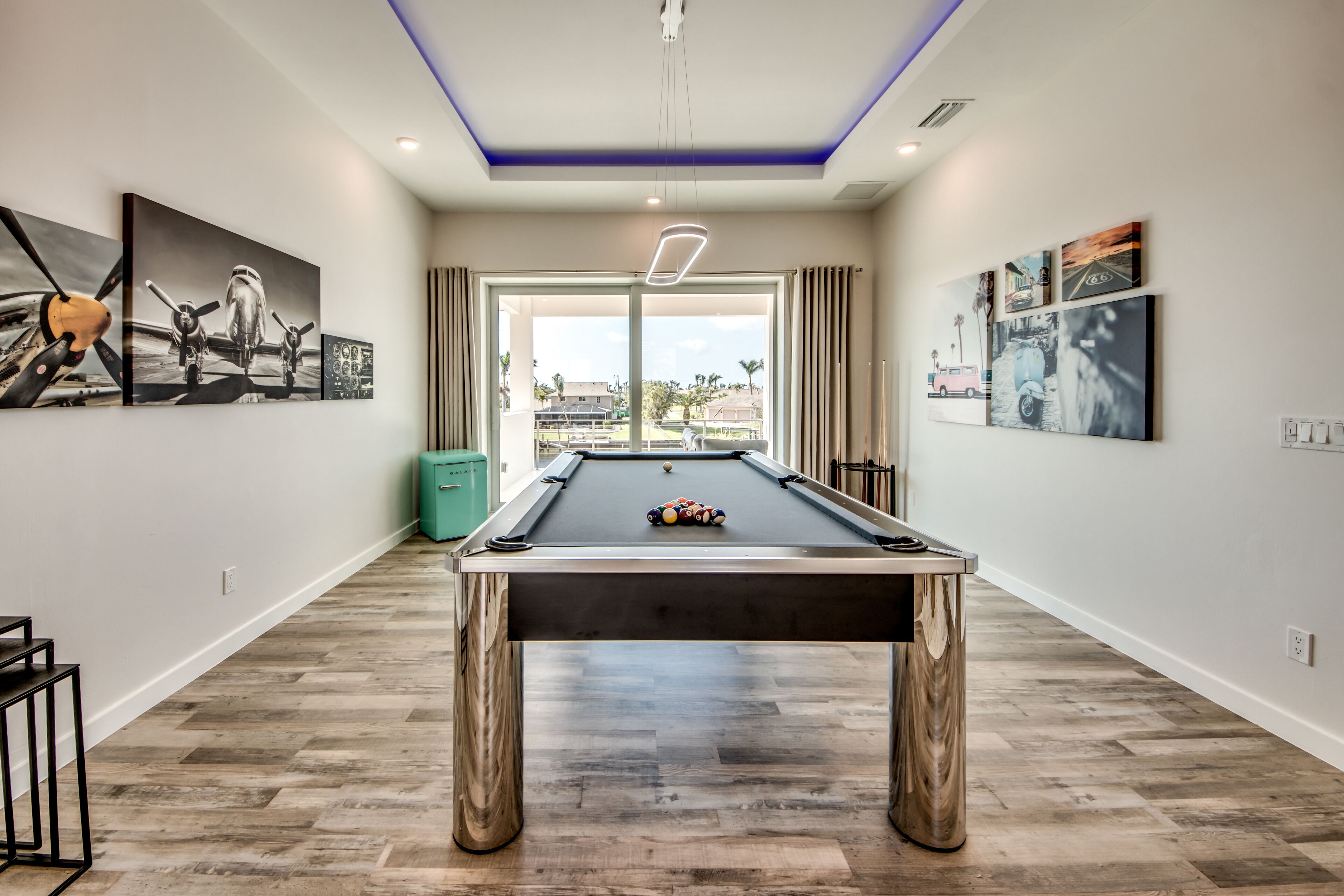 A pool table in a modern room with wooden flooring, a ceiling light, and artwork on the walls.