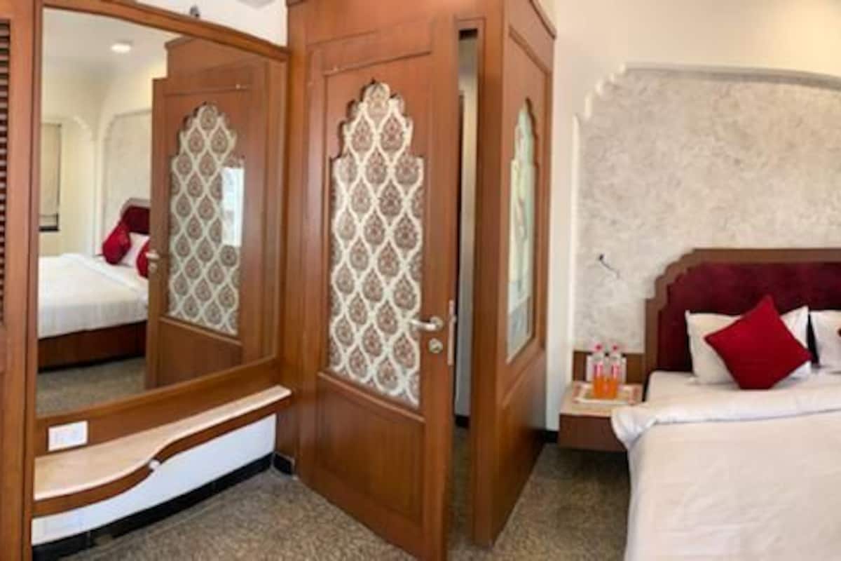 Quarto de hotel com uma cama grande, um guarda-roupa de madeira, um espelho e uma janela com vista.