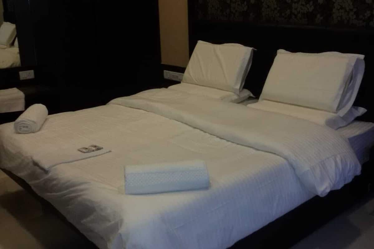 Uma cama de casal com lençóis e almofadas brancos, uma toalha dobrada e um controle remoto na cama.