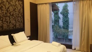 Habitación de hotel con una cama grande, una ventana con cortinas y vistas a árboles.