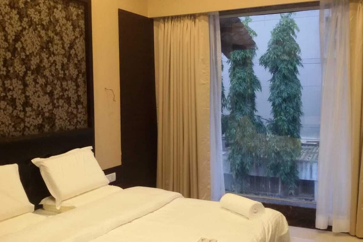 Quarto de hotel com uma cama grande, janela com cortinas e vista para árvores.
