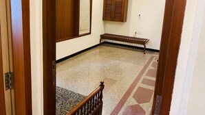 Una habitación con suelo de madera, un banco, un armario y una ventana con persiana.