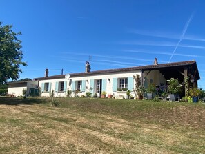 Uma casa de dois andares com uma varanda frontal grande, antena parabólica e vasos de plantas.