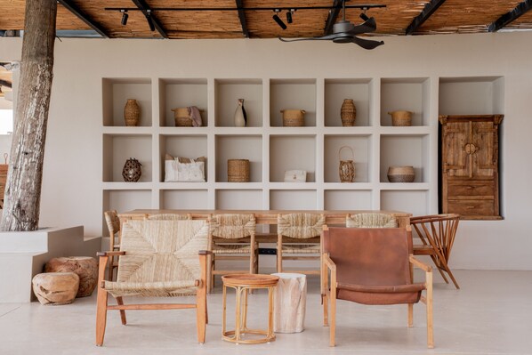 A room with a wooden ceiling, a large white shelving unit with various baskets and containers, and a seating area with wicker chairs and a brown leather chair. - Gaia By The Sea - Adult Only (Çesme)