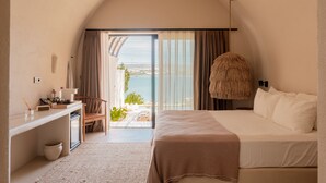 A bedroom with a large bed, a desk with a chair, a hanging light fixture, and a view of the sea through a glass door. - Gaia By The Sea - Adult Only (Çesme)