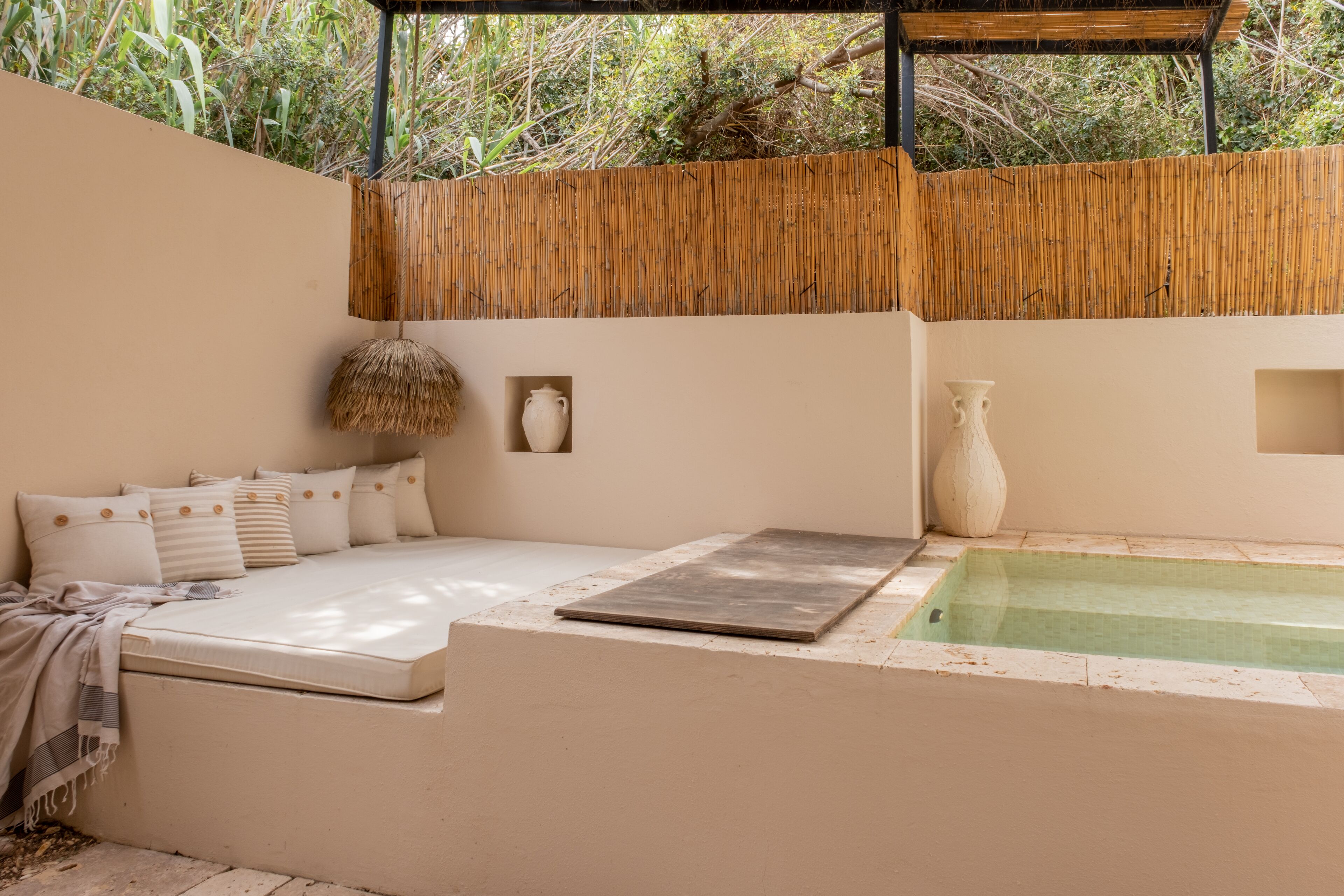 A minimalist outdoor seating area with a cushioned bench, a small table, and a decorative hanging element.