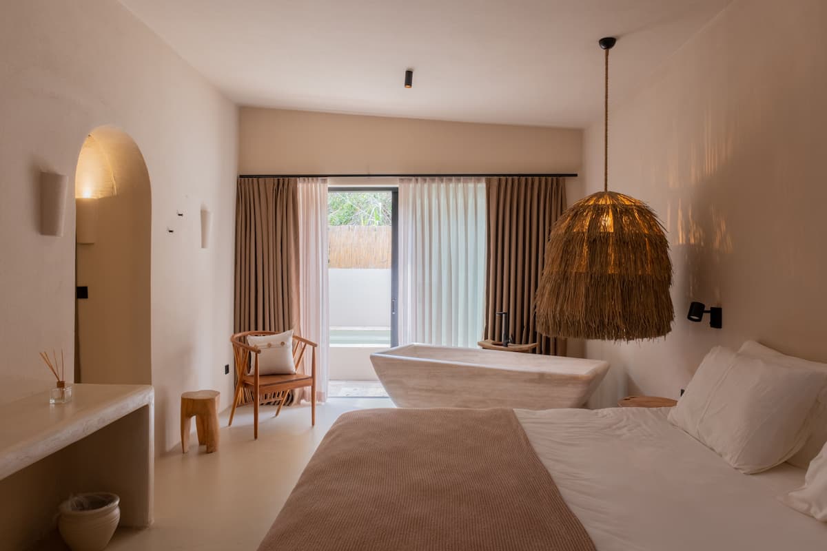 A hotel room with a large bed, a smaller bed, a wooden chair, a small stool, a nightstand, and a hanging lamp.