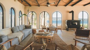 A spacious living room with a sofa, round coffee table, and wicker chairs. Large arched windows offer a view of the sea. - Gaia By The Sea - Adult Only (Çesme)