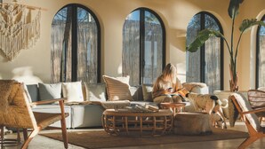 A cozy living room with a sofa, chairs, and a coffee table. There are large windows with curtains, and a plant is visible. - Gaia By The Sea - Adult Only (Çesme)