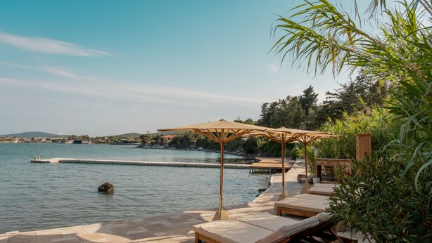 A waterfront patio with lounge chairs and umbrellas, overlooking a calm body of water. - Gaia By The Sea - Adult Only (Çesme)