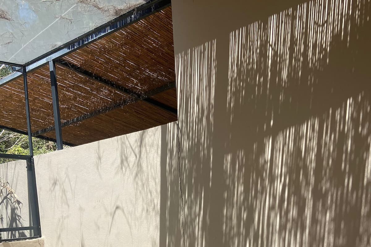 A sunlit outdoor seating area with a stone bench and cushions, a small pool, and a pergola overhead.