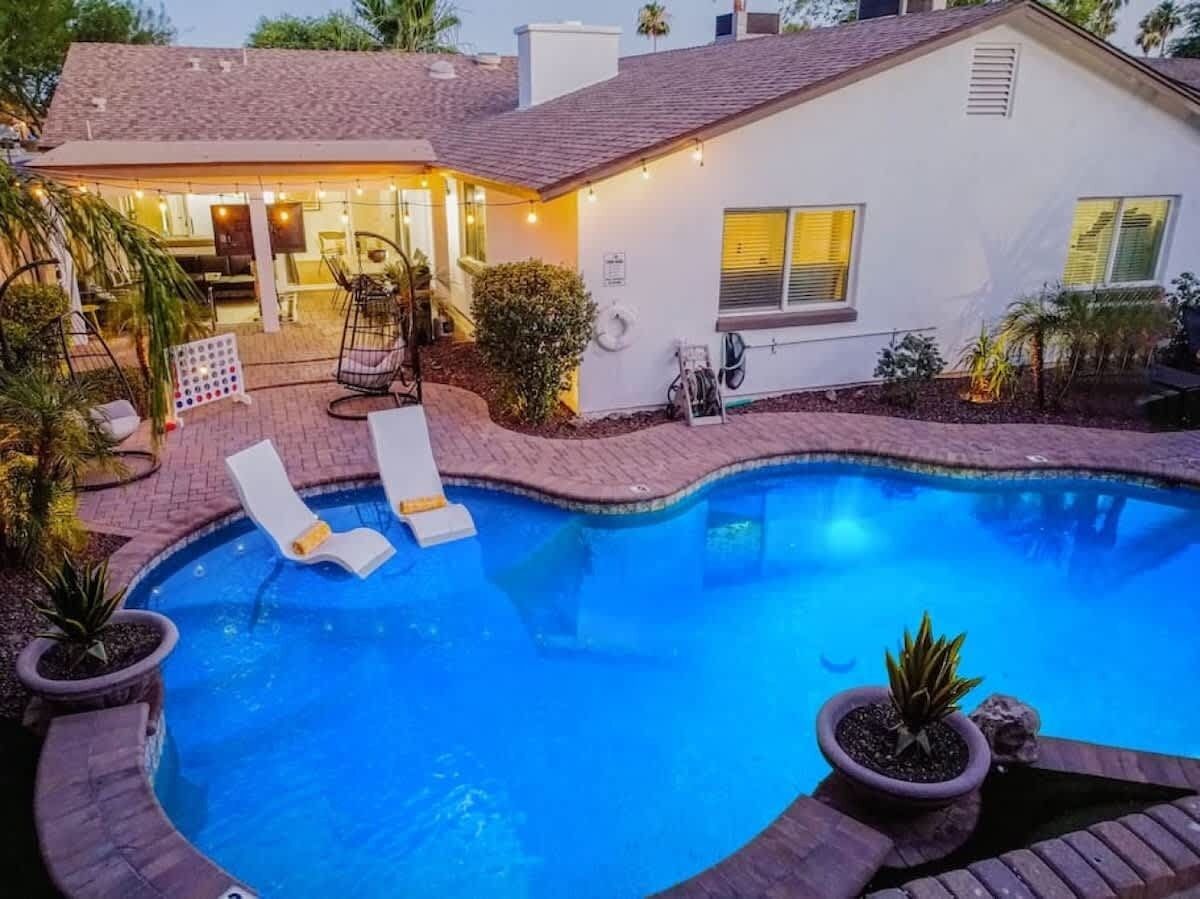 Une piscine avec des chaises longues, un patio couvert et une maison blanche à l’extérieur en briques.