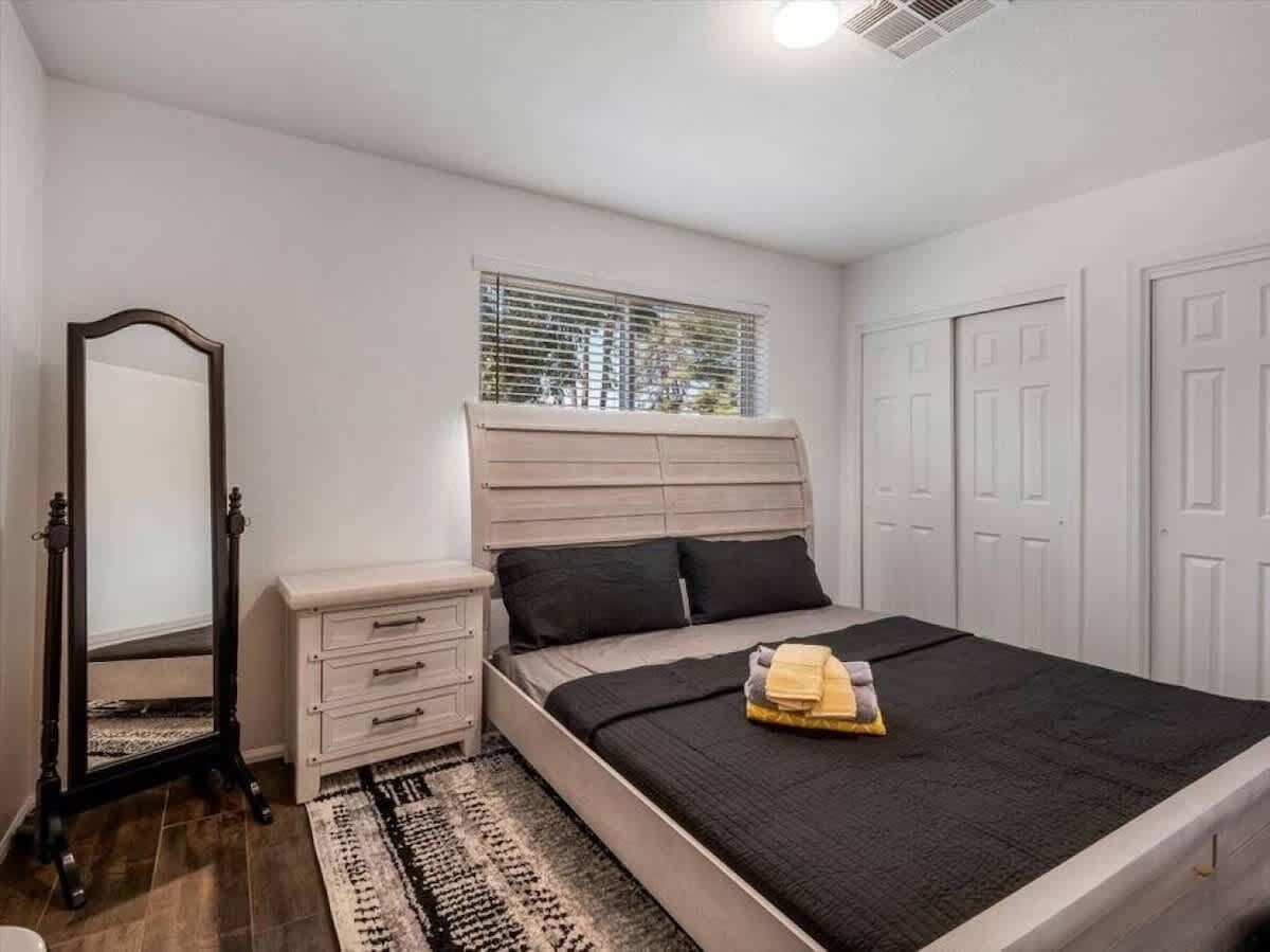 A bedroom with a bed, a dresser, a mirror, and a window with blinds.