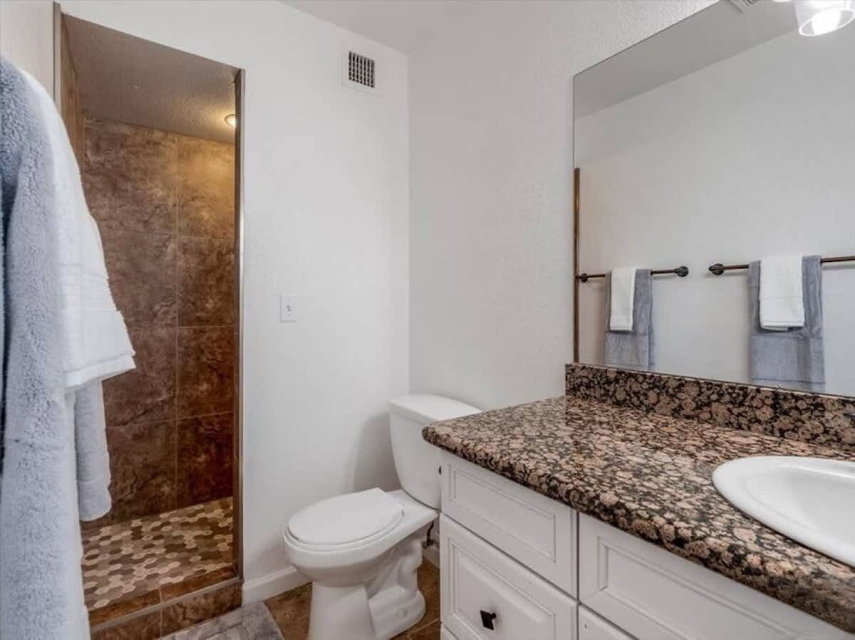 A bathroom with a shower, toilet, sink, and a mirror.