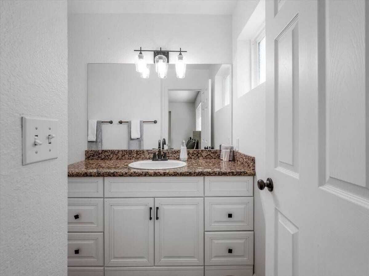 A bathroom with a white vanity, a granite countertop, a mirror, and a three-light fixture above the sink.