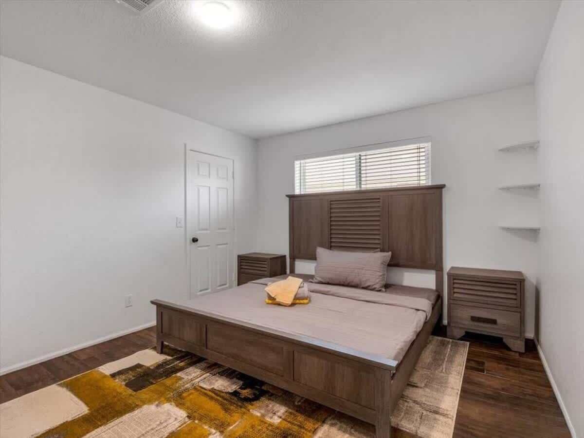 A bedroom with a bed, bedside tables, a window with blinds, and a door.