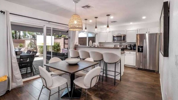 Une cuisine moderne avec des meubles blancs, des appareils en acier inoxydable et un coin repas comprenant une table et des chaises.