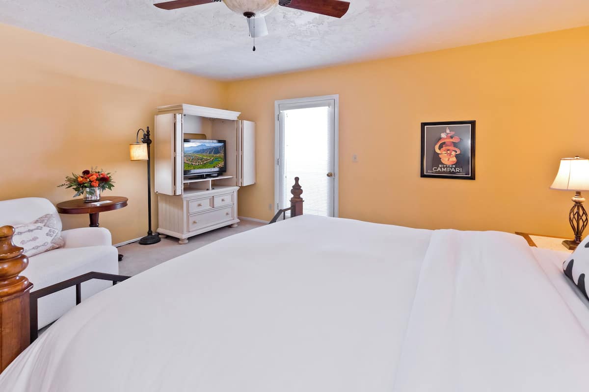 A hotel room with a bed, a TV on a cabinet, a lamp, and a framed picture on the wall.