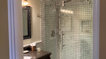 Un baño con ducha envuelta en vidrio, tocador con espejo e inodoro.