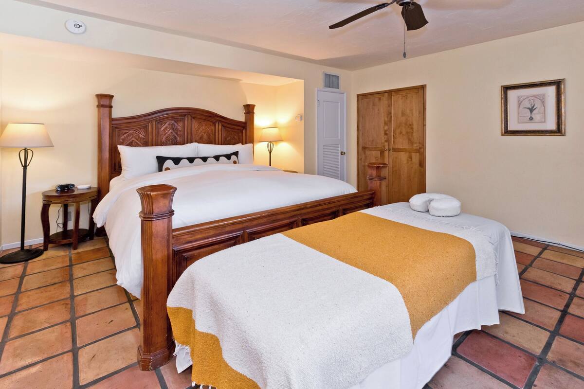 A neatly made bed with a wooden headboard, a bedside lamp, and a towel on the floor.