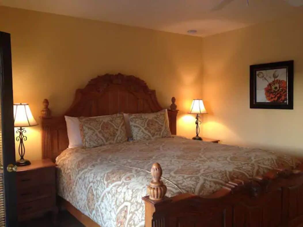 A neatly made bed with a patterned bedspread, two bedside lamps, and a framed picture on the wall.