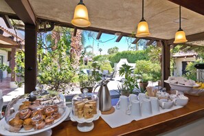 Un bufé de desayuno con pasteles y café, con un fondo de vegetación exuberante y cielo despejado.