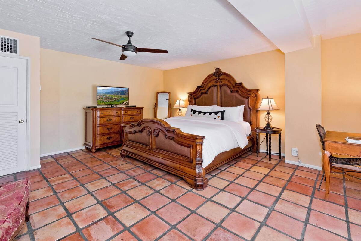 A bedroom with a wooden bed, a ceiling fan, a dresser, a desk, and a chair.
