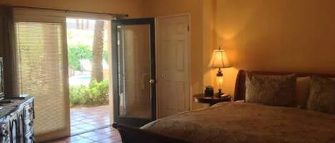 A bedroom with a bed, a nightstand, a lamp, a ceiling fan, and a door leading to an outdoor area.