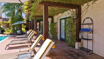 A poolside area with lounge chairs, a pool, and a pergola covered in greenery.