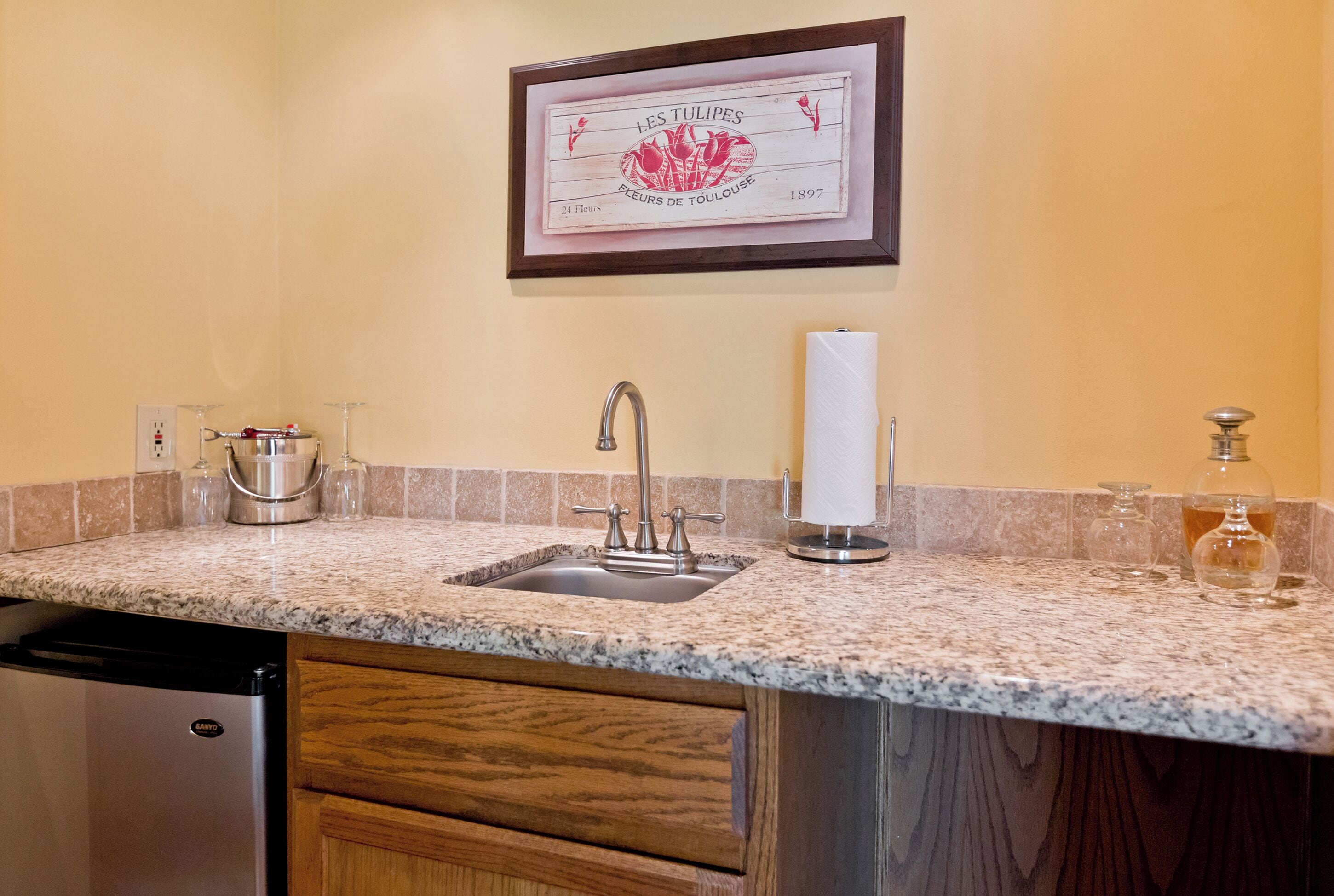 Una cocina con encimeras de granito, un fregadero de acero inoxidable, armarios de madera y un certificado enmarcado en la pared.