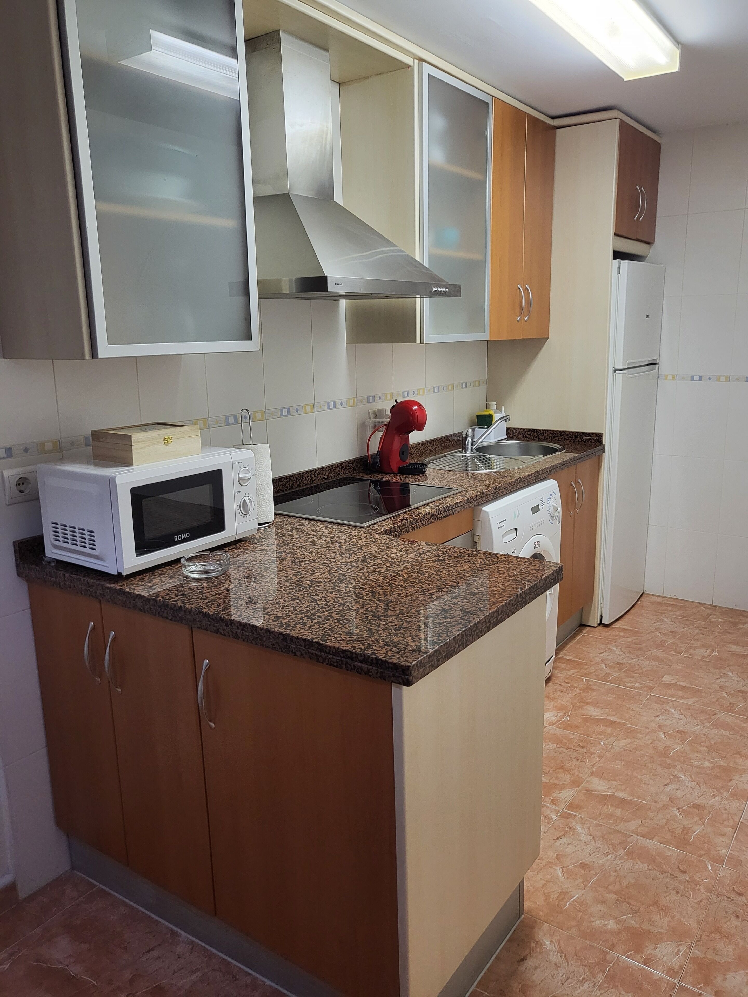 A kitchen with a microwave, a red mixer, a sink, and a refrigerator.