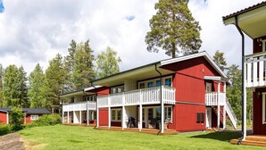 A red two-story building with a white balcony, surrounded by a grassy yard and trees.