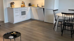 A modern kitchen with white cabinetry, a microwave, and a refrigerator. There's a dining area with a table and chairs.