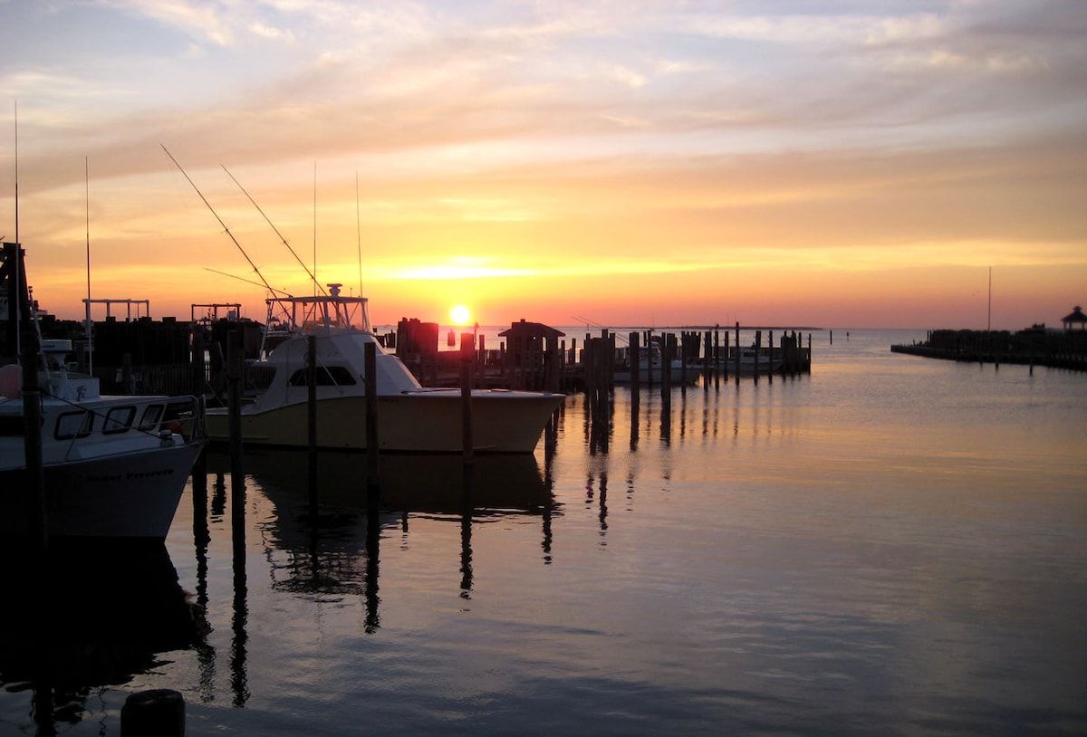 A marina with boats docked, calm water, and a sunset in the background.