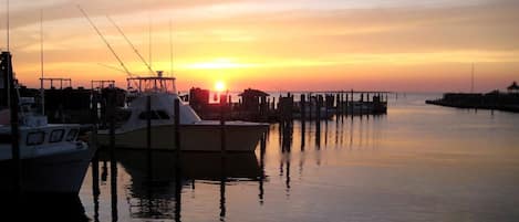 A marina with boats docked, calm water, and a sunset in the background.