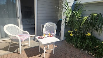 A patio with two white wicker chairs, a small table, and a potted plant.