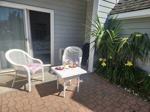 A patio with two white wicker chairs, a small table, and a potted plant.