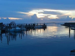 A marina with boats docked at wooden piers, calm water, and a sunset in the background. - Charming one bedroom condo with private patio. HI-101 (Hatteras)