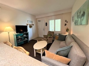 A living room with a sofa, a television, a lamp, and a window. - Charming one bedroom condo with private patio. HI-101 (Hatteras)